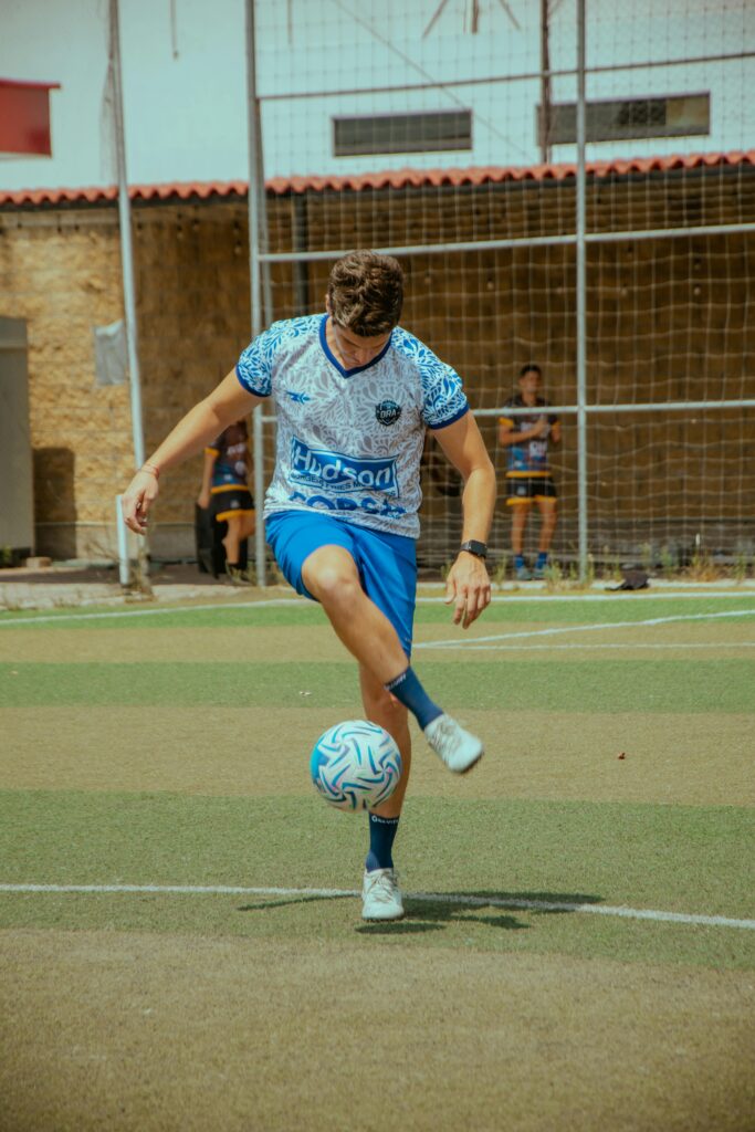Young man skillfully juggling a soccer ball on an outdoor field during the day.