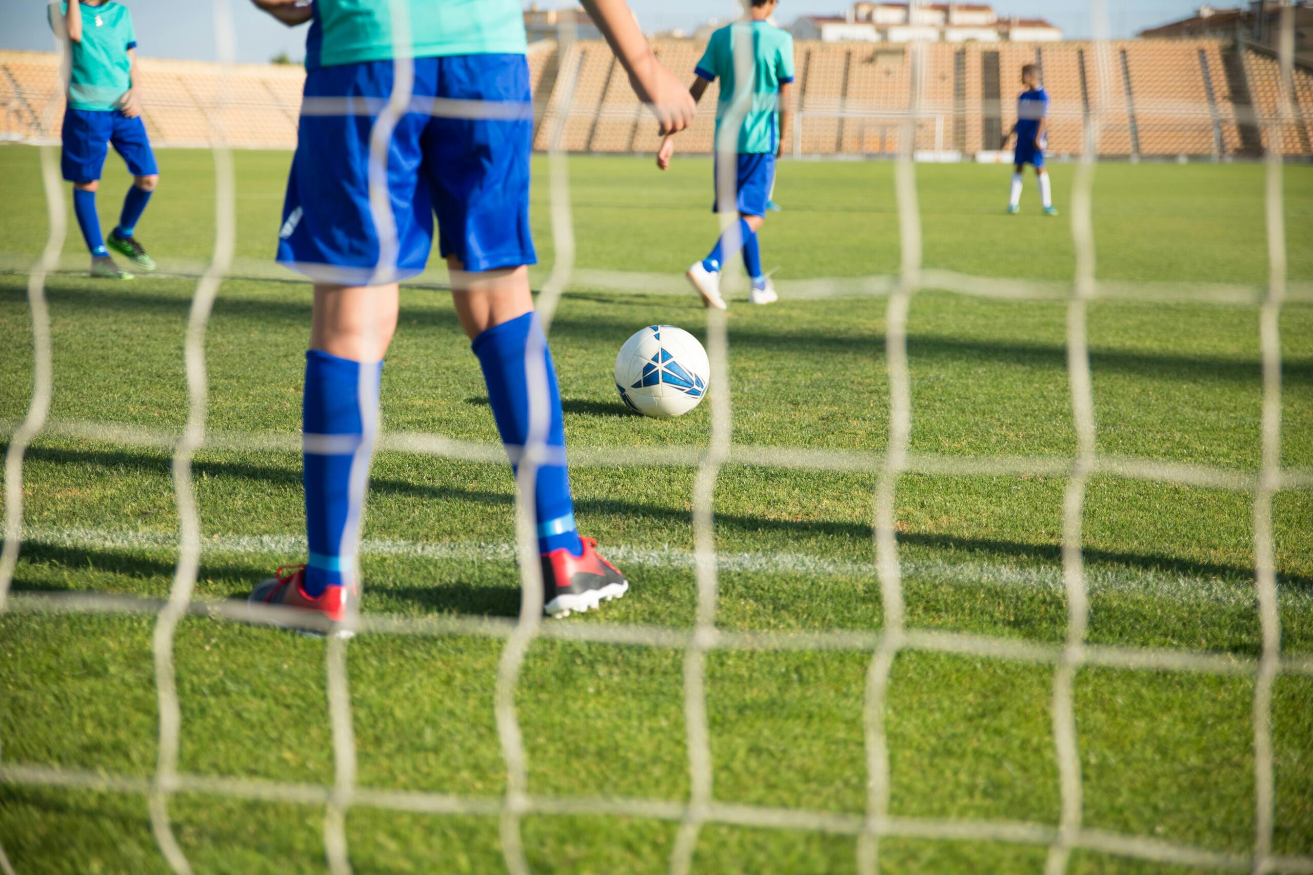 Children playing soccer outdoors on a sunny day in a Portuguese stadium.