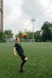 Woman athlete skillfully balances a soccer ball on a field during a daytime practice. Learns how to juggle a soccer ball.